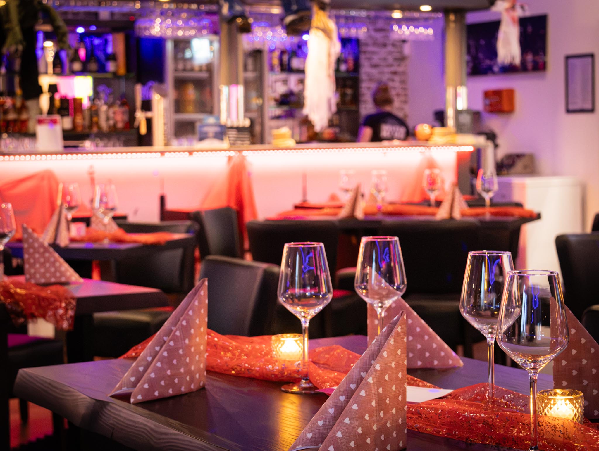 Gedeckte Tische vor der beleuchteten Bar